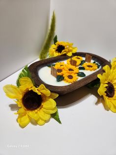 some sunflowers are sitting on a table next to a wooden tray with milk