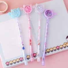 three pens sitting on top of an open notebook next to a pair of pink scissors