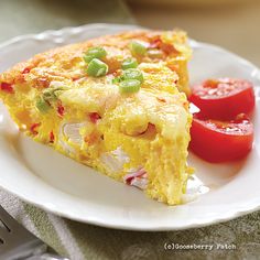 a slice of quiche on a white plate with tomatoes and green onions next to it