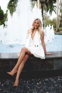 a beautiful woman sitting on top of a fountain in front of a fountain with water