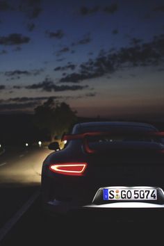 the back end of a sports car at night with its lights on and tail light turned on