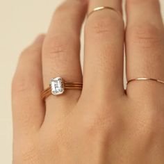 a woman's hand wearing a gold ring with a white diamond in the middle