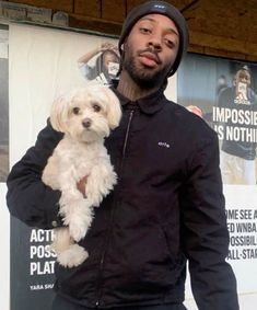 a man holding a small white dog in his arms while standing next to a sign