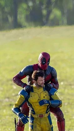 two people dressed as deadpool and spider - man are standing in front of a grassy field