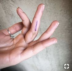 a person's hand with a tiny purple flower tattoo on their thumb and fingers