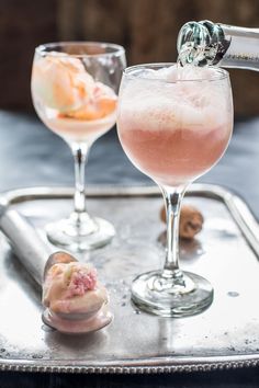 two glasses filled with different types of drinks on top of a metal tray next to each other