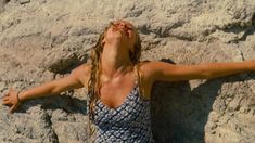 a woman in a blue and white dress standing next to a rock formation with her arms outstretched