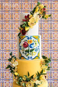 a three tiered cake decorated with flowers and leaves on a yellow tablecloth background