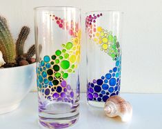 two colorful glasses sitting on top of a table next to a cactus