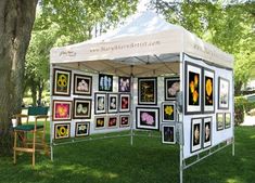 a white tent with pictures on it in the grass under a tree and some chairs