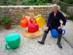 a woman sitting on a bench next to some colorful pots and jugs in front of a stone wall