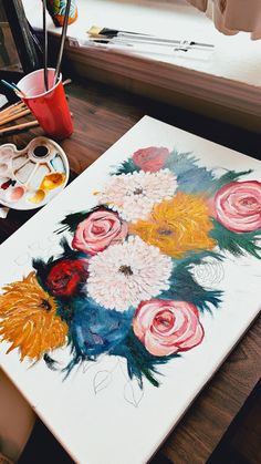 a painting with flowers on it next to some paintbrushes and other art supplies