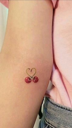 two cherries in the shape of a heart tattoo on the left side of the arm