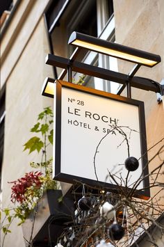 a hotel sign hanging from the side of a building next to a tree with flowers