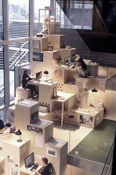 people are sitting at desks in a room with shelves and boxes on the floor