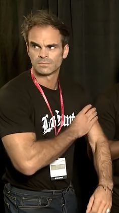 a man standing in front of a black curtain with his arms crossed and looking at the camera