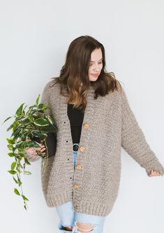 a woman holding a potted plant and wearing a brown cardigan over her shoulder