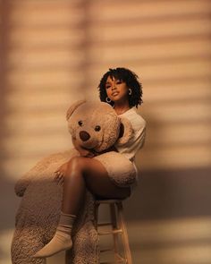 a woman sitting on top of a stool holding a large teddy bear in her arms