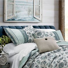 a bed with blue and white comforters, pillows and blankets on top of it