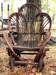 an old wooden rocking chair sitting in the grass next to a tree with fallen leaves on it