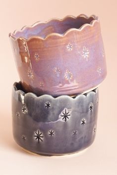 three ceramic bowls sitting side by side on a pink tableclothed surface, one with silver stars and the other has purple glaze