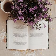 an open book sitting on top of a table next to a cup of coffee and flowers