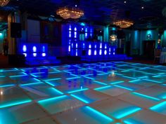 a dance floor is lit up with blue lights in the center and white tiles on it