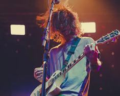 a man with long hair playing an electric guitar at a concert in front of microphones