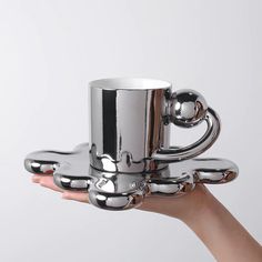 a hand holding a silver coffee cup in the shape of a robot's arm