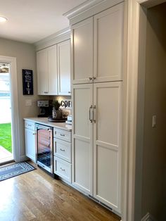 a kitchen with white cabinets and wood flooring next to an open door that leads to a patio