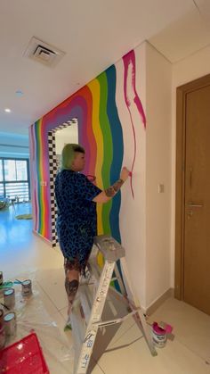 a woman is painting a rainbow wall in the living room with her feet on a ladder