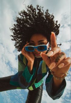 a woman wearing sunglasses making the peace sign with her hand while standing under a cloudy blue sky