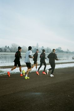 a group of people running down a street next to a lake with snow on the ground