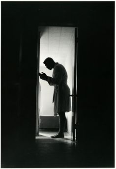 a man standing in an open doorway looking at his cell phone while wearing a robe