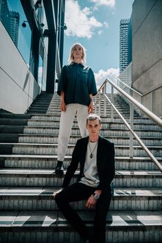 two people sitting on the steps in front of some stairs with their heads tilted to the side