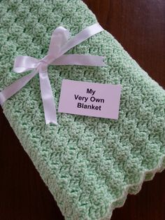 a green crocheted blanket with a white ribbon on it that says, my very own blanket