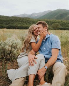 a man and woman are sitting in the grass with their arms around each other as they hug