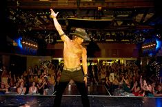 a shirtless man on stage with his arms in the air while people watch him