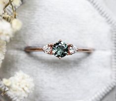 an engagement ring with three stones on it and white flowers in the back ground behind it