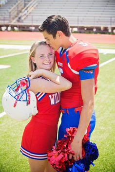 a man and woman in cheerleader uniforms hugging on the field at a football game