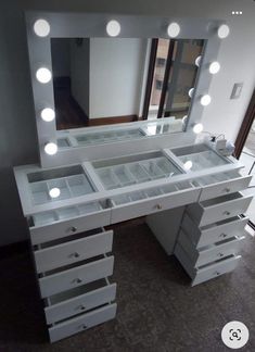 a white vanity with lighted drawers and lights on it's sides, in front of a window