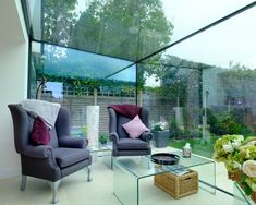 a living room with two chairs and a glass table in front of the window that has flowers on it