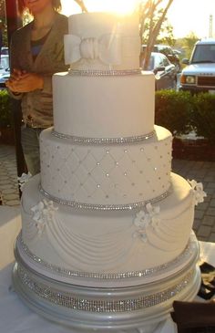 a large white wedding cake sitting on top of a table next to a woman standing behind it