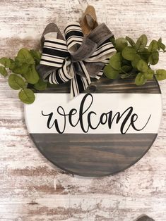 a welcome sign hanging on the side of a wooden wall with greenery in it