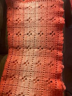 an orange crocheted blanket sitting on top of a couch next to a pillow