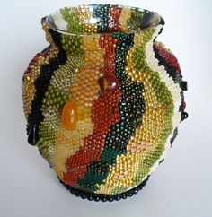 a multicolored vase is sitting on a white surface with beading around it