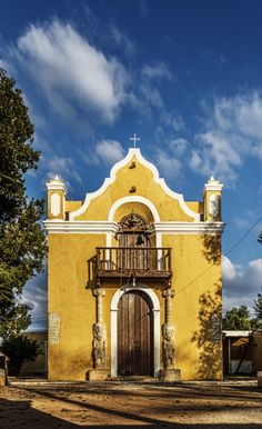 a yellow church with a brown door and balcony