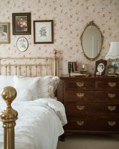 a bedroom with pink wallpaper and white bedding, gold headboard and foot board