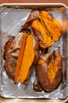 baked sweet potatoes sitting on top of aluminum foil in a pan with one cut in half