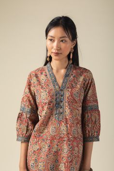 This rust-colored cotton kurta features a vibrant multi-color Kalamkari print, adding an artistic flair. The yoke is elegantly highlighted with a border, sequins, mirror work, buttons, and intricate thread detailing. It has a stylish V-neck collar, 3/4th sleeves adorned with a border and crochet lace, and a convenient side pocket. The straight fit design ensures both comfort and a flattering silhouette.. Pair it with our cotton pant for a cohesive look that exudes confidence. Kurta With Collar Women, V Neck Collar Kurta, Straight Kurti Designs Cotton, Ikat Kurti Designs, Kurta Sleeves Design, Kalamkari Kurti Designs, Kalamkari Kurta Designs